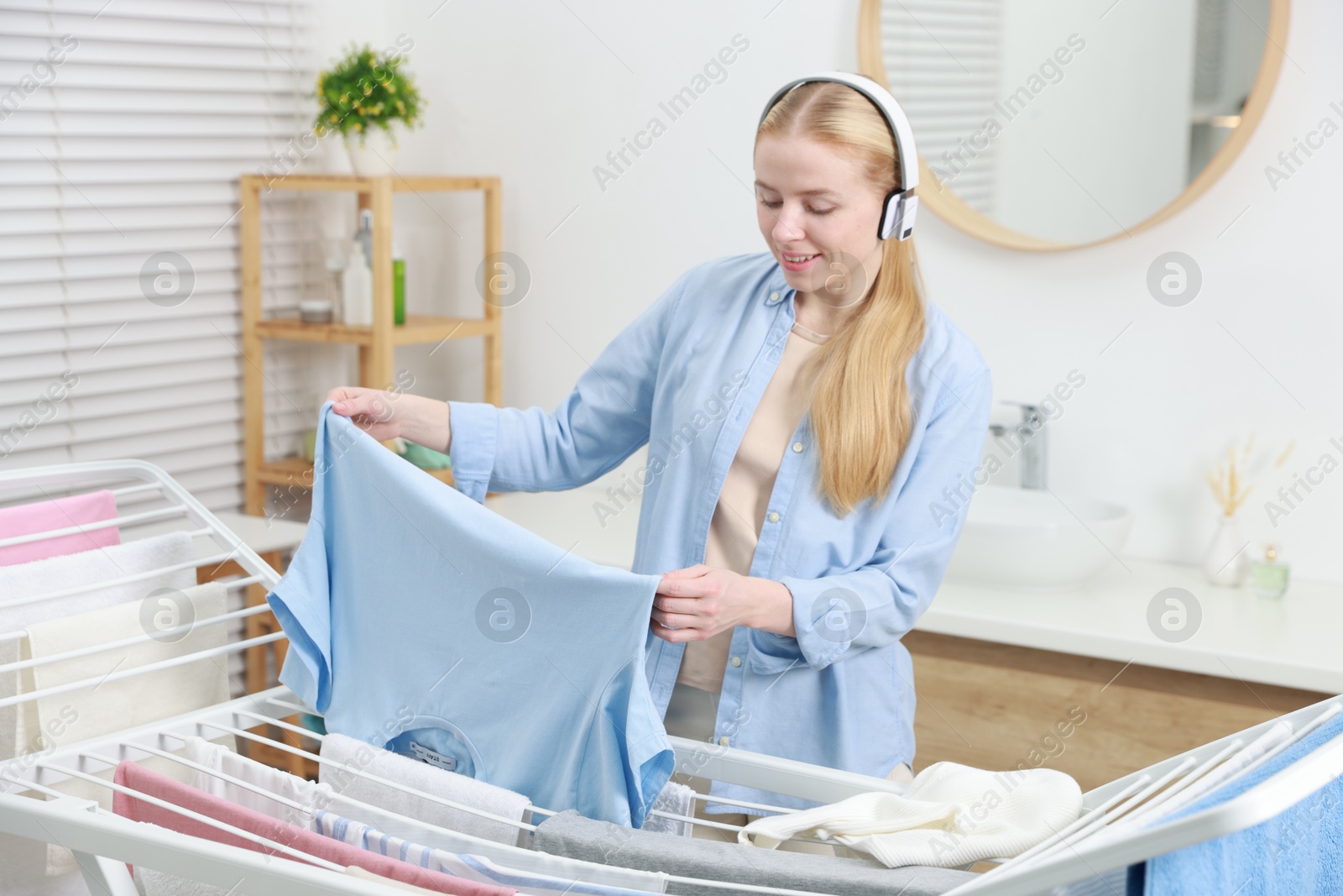 Photo of Woman listening to music while hanging fresh laundry on drying rack at home