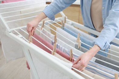 Photo of Woman hanging fresh clean laundry on drying rack at home, closeup