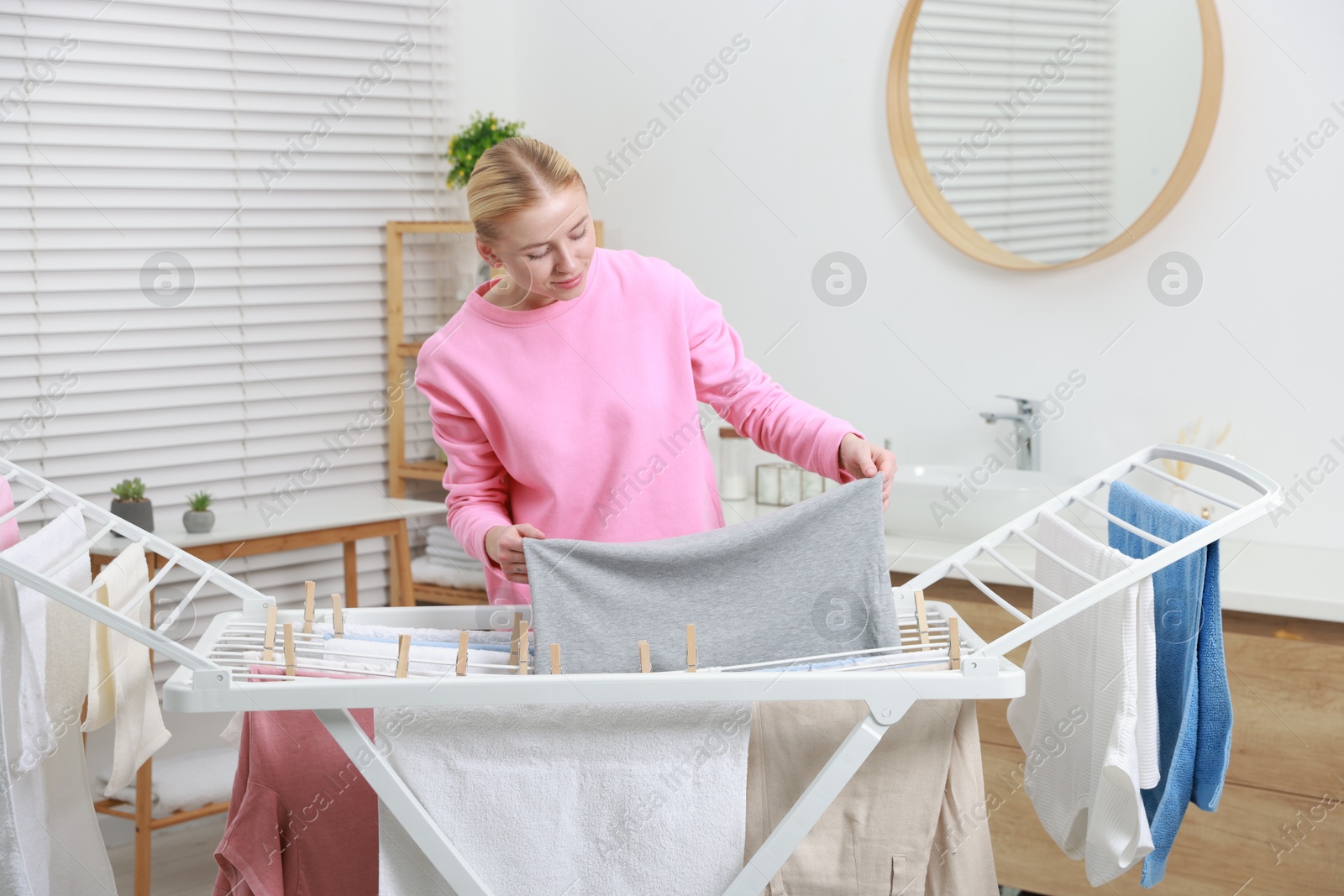 Photo of Beautiful woman hanging fresh clean laundry on drying rack at home