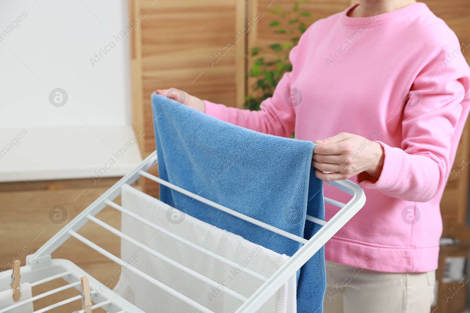 Photo of Woman hanging fresh clean laundry on drying rack at home, closeup