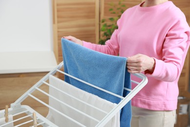 Photo of Woman hanging fresh clean laundry on drying rack at home, closeup