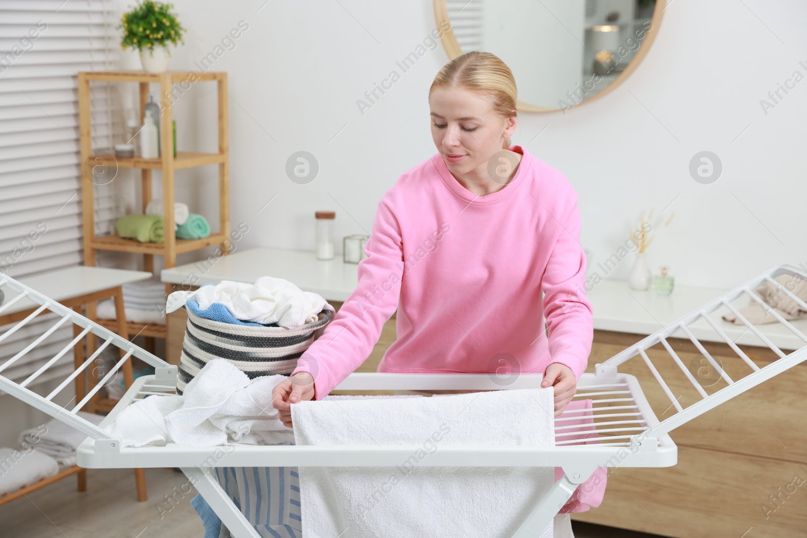 Photo of Beautiful woman hanging fresh clean laundry on drying rack at home