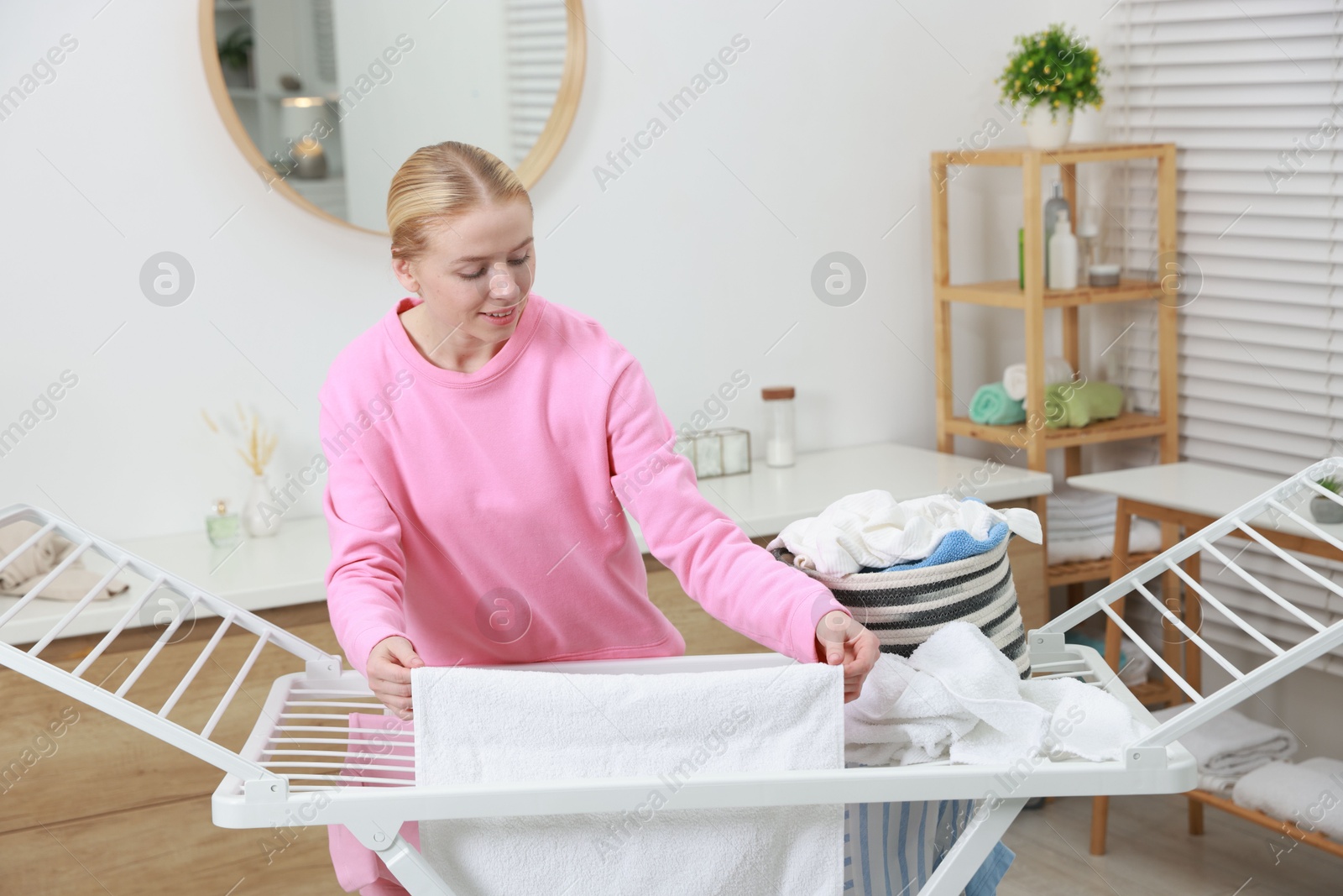 Photo of Beautiful woman hanging fresh clean laundry on drying rack at home