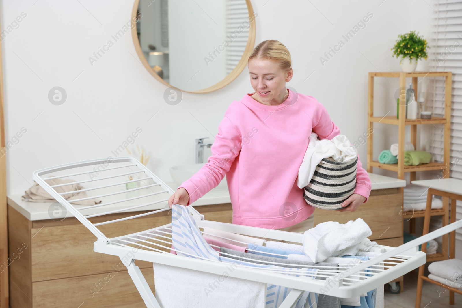 Photo of Beautiful woman hanging fresh clean laundry on drying rack at home