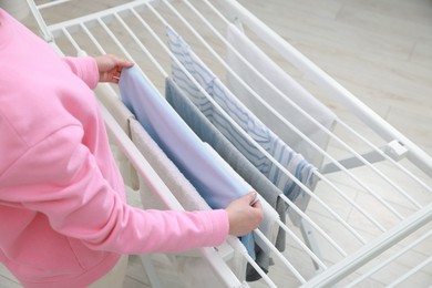 Photo of Woman hanging fresh clean laundry on drying rack at home, closeup