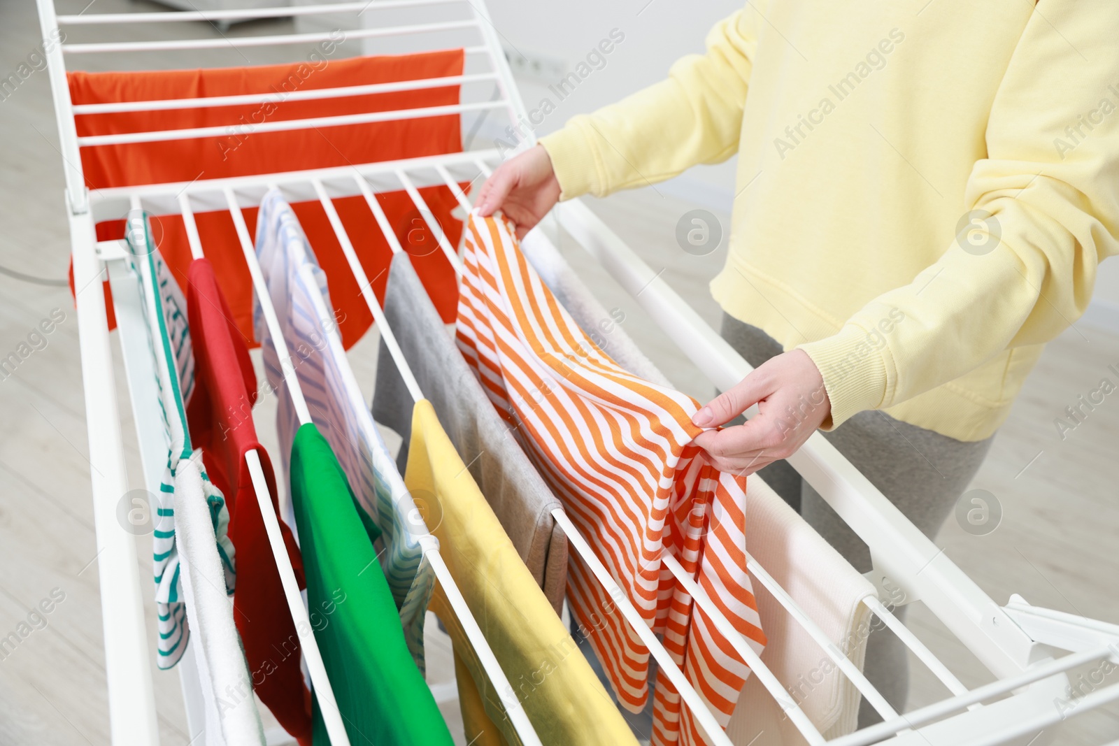 Photo of Woman hanging fresh clean laundry on drying rack at home, closeup