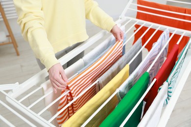 Photo of Woman hanging fresh clean laundry on drying rack at home, closeup