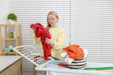 Photo of Beautiful woman hanging fresh clean laundry on drying rack at home