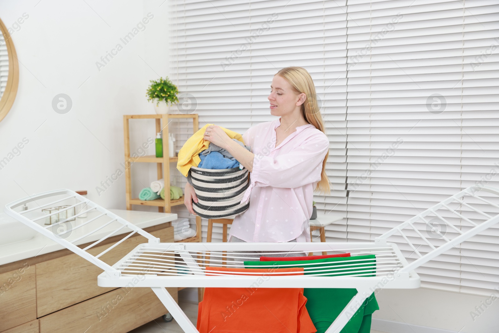 Photo of Beautiful woman hanging fresh clean laundry on drying rack at home