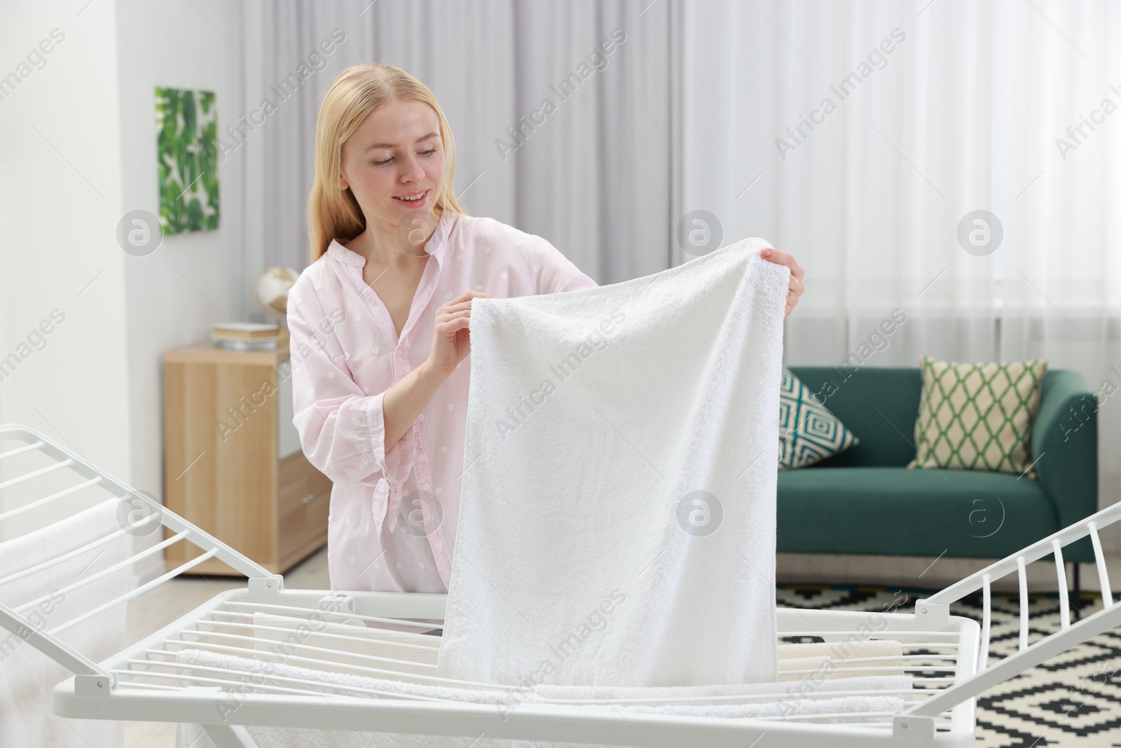 Photo of Beautiful woman hanging fresh clean laundry on drying rack at home