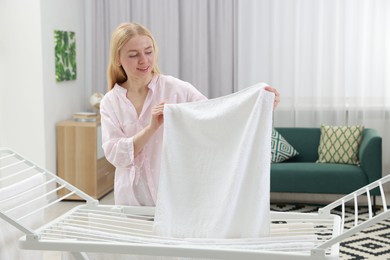 Photo of Beautiful woman hanging fresh clean laundry on drying rack at home