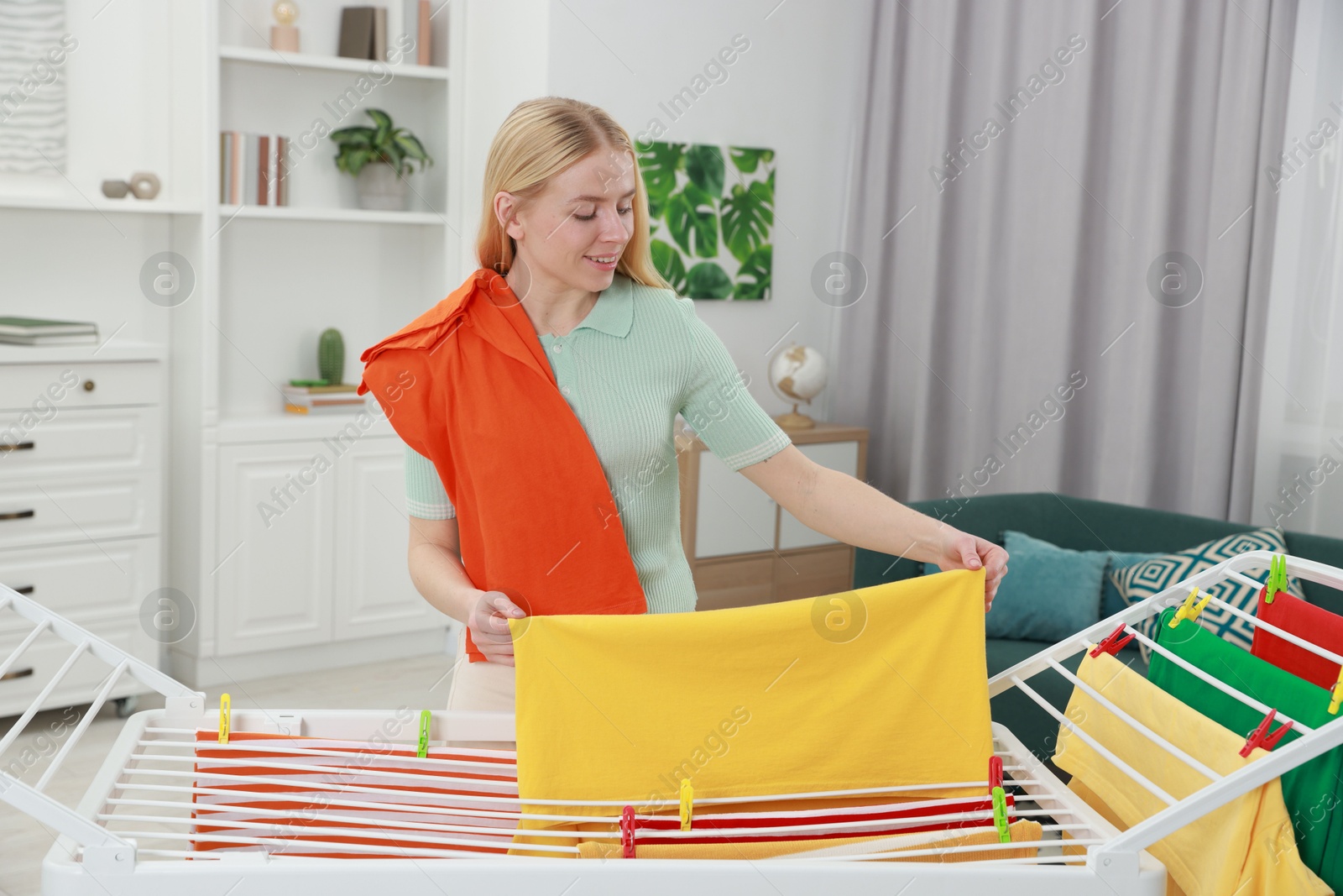 Photo of Beautiful woman hanging fresh clean laundry on drying rack at home