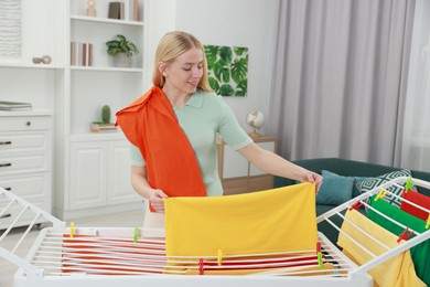 Photo of Beautiful woman hanging fresh clean laundry on drying rack at home