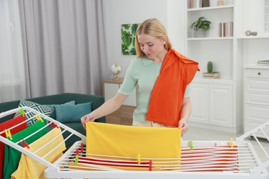 Photo of Beautiful woman hanging fresh clean laundry on drying rack at home