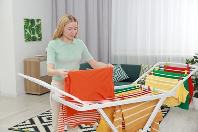 Photo of Beautiful woman hanging fresh clean laundry on drying rack at home