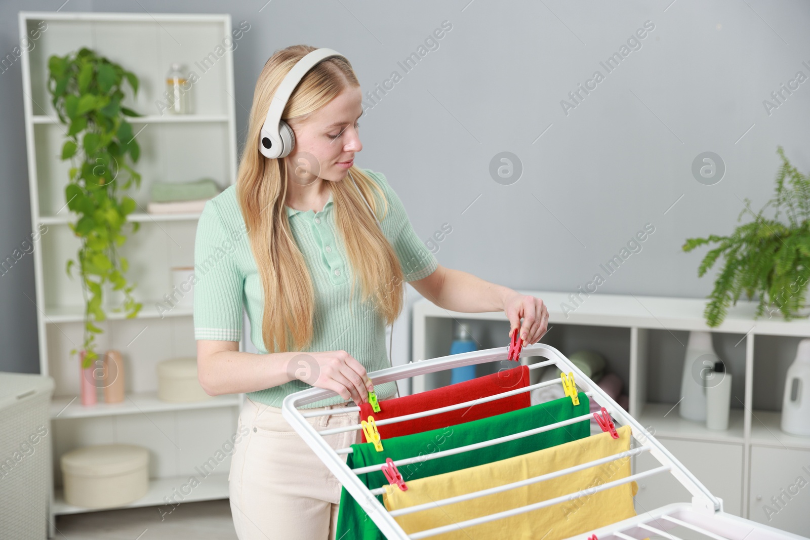 Photo of Woman listening to music while hanging fresh laundry on drying rack at home