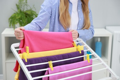 Photo of Woman hanging fresh clean laundry on drying rack at home, closeup