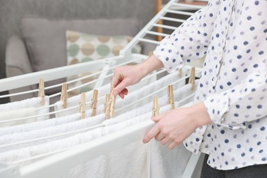 Photo of Woman hanging fresh clean laundry on drying rack at home, closeup