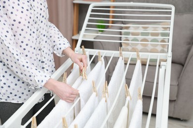 Photo of Woman hanging fresh clean laundry on drying rack at home, closeup