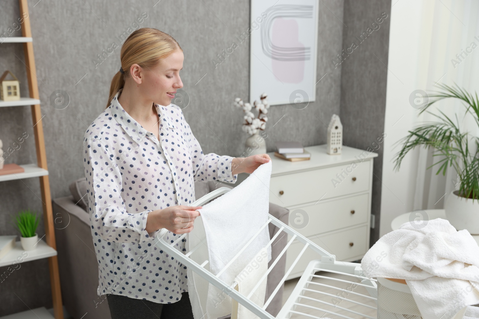 Photo of Beautiful woman hanging fresh clean laundry on drying rack at home