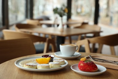 Photo of Delicious cottage cheese pancakes, dessert and coffee served on wooden table in cafe