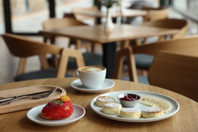 Photo of Delicious cottage cheese pancakes, dessert and coffee served on wooden table in cafe