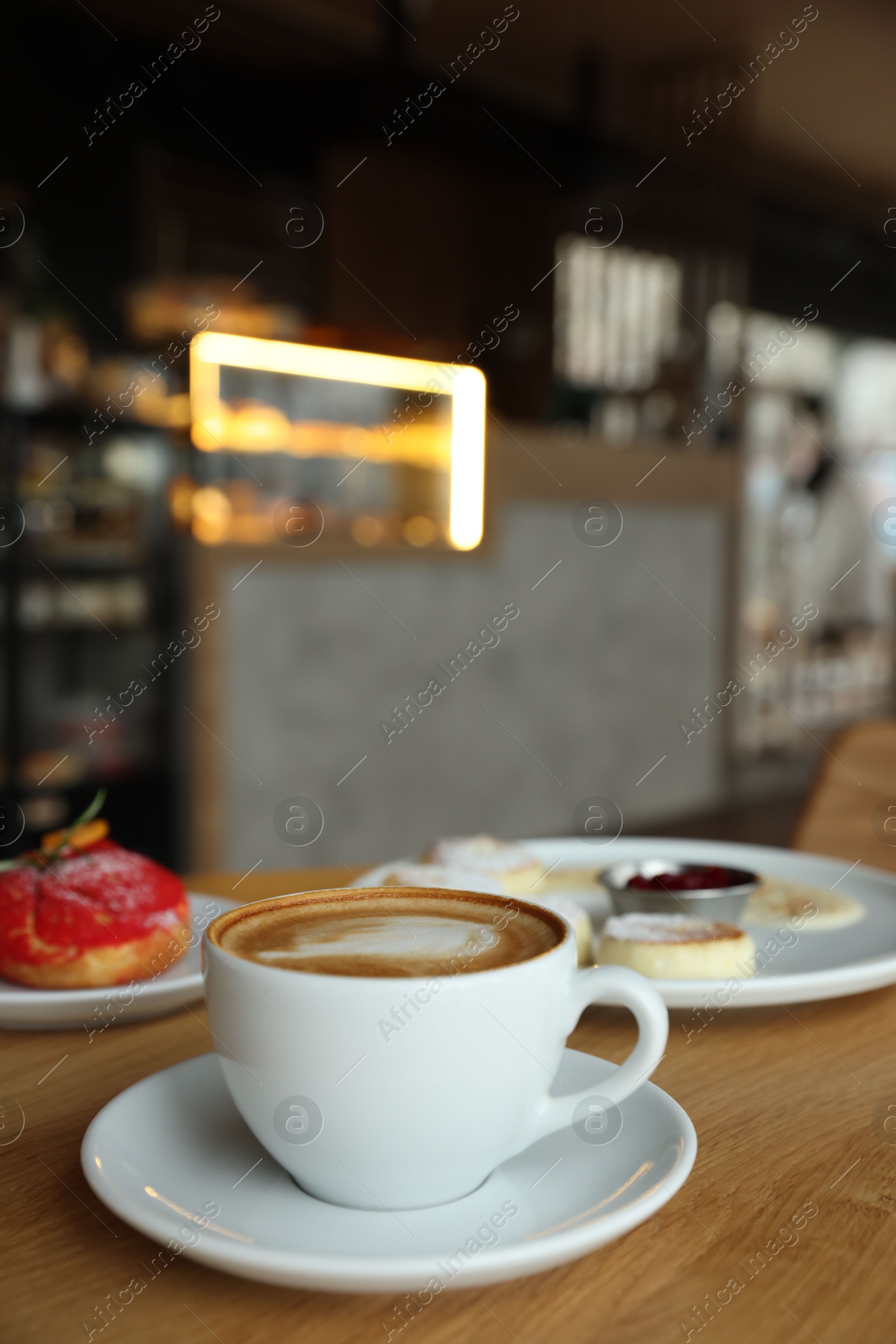 Photo of Aromatic cappuccino, delicious cottage cheese pancakes and dessert served on wooden table in cafe, closeup