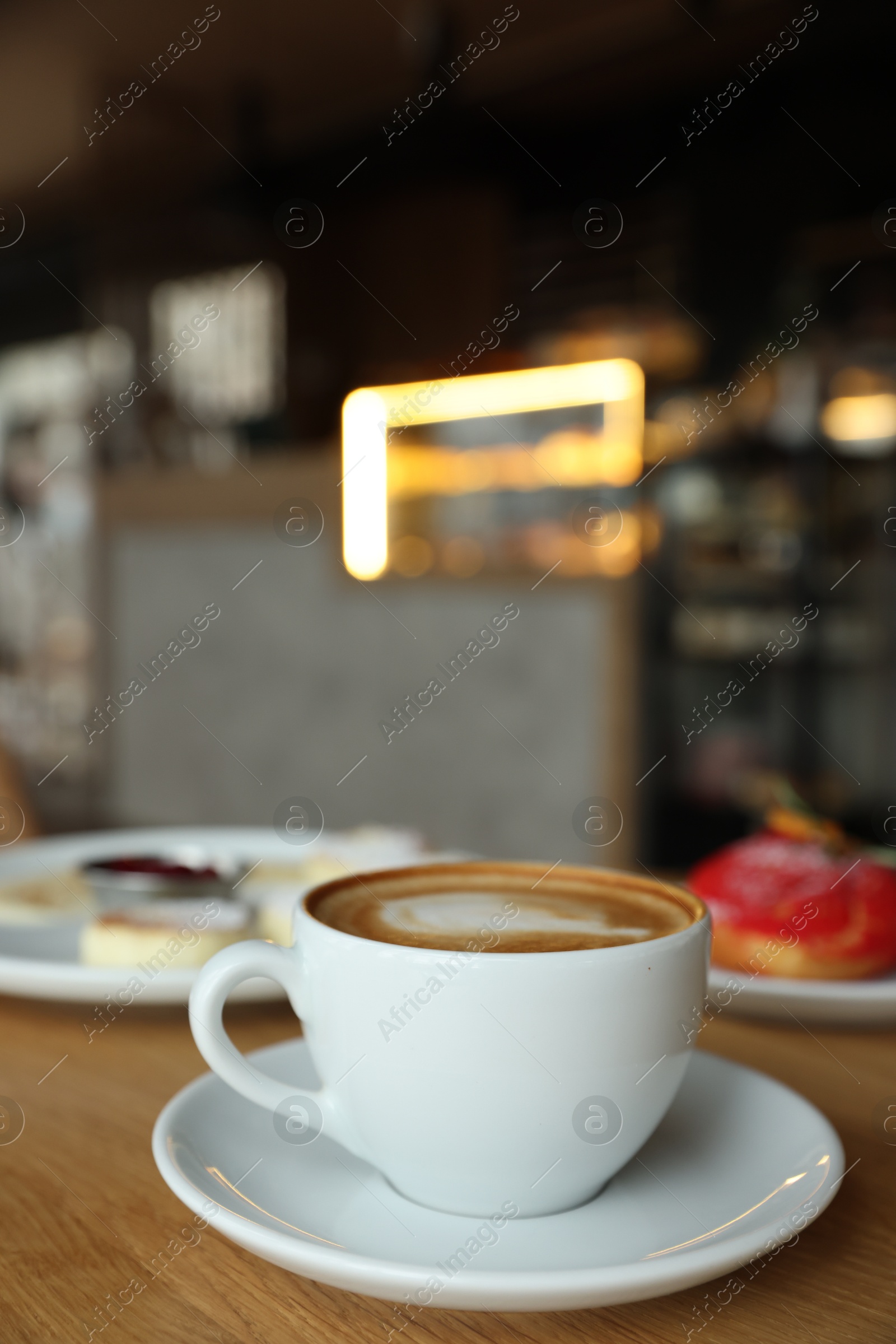 Photo of Aromatic cappuccino, delicious cottage cheese pancakes and dessert served on wooden table in cafe, closeup