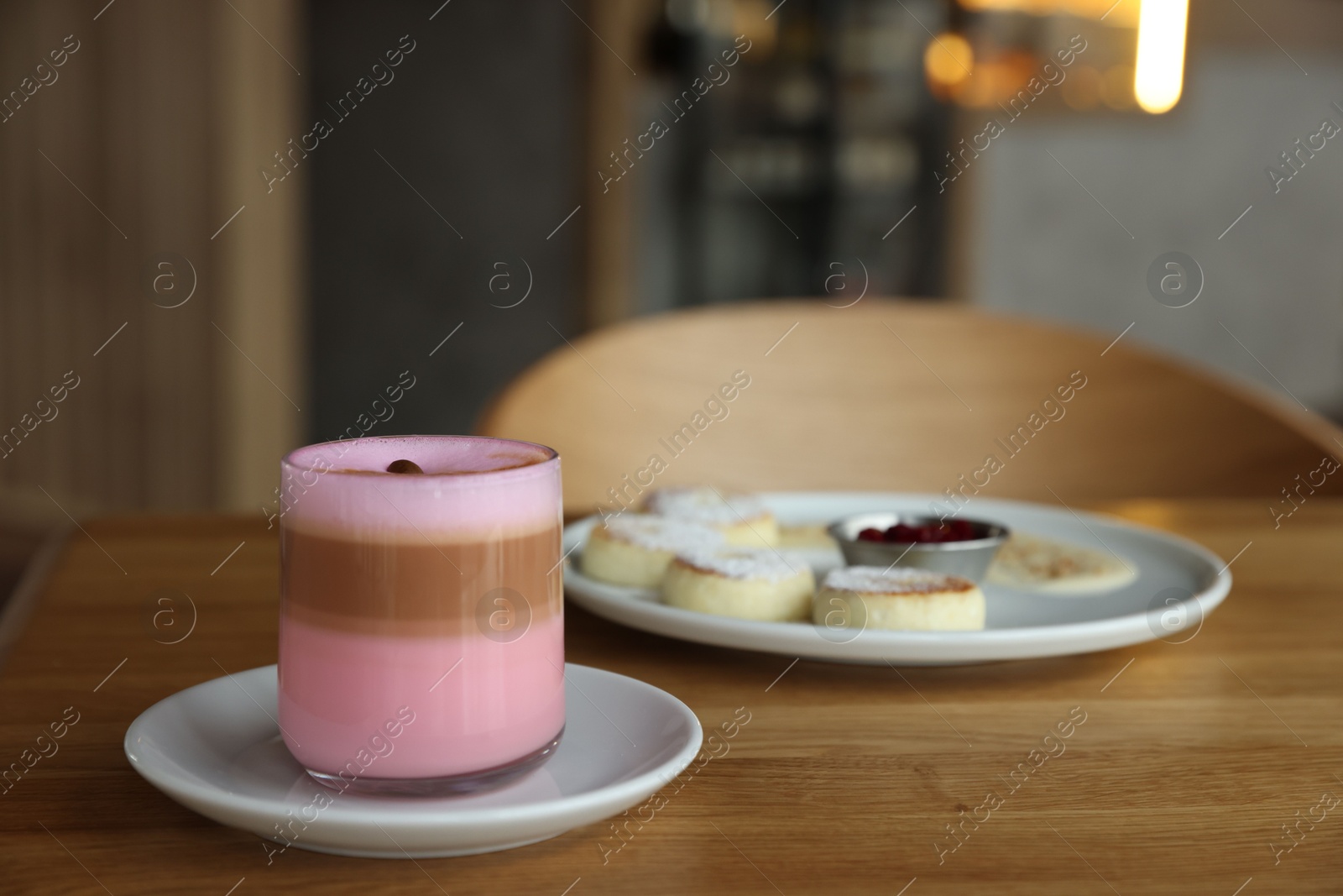 Photo of Delicious cottage cheese pancakes and pink latte served on wooden table indoors