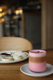 Photo of Delicious cottage cheese pancakes and pink latte served on wooden table indoors