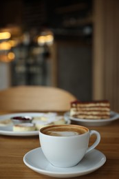 Photo of Aromatic coffee and delicious desserts served on wooden table in cafe, closeup