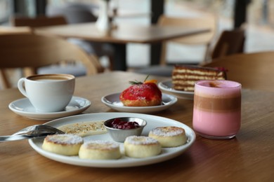 Photo of Delicious cottage cheese pancakes, desserts and aromatic coffee served on wooden table in cafe