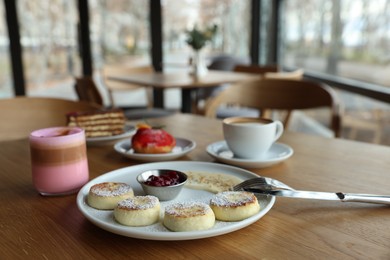 Photo of Delicious cottage cheese pancakes, desserts and aromatic coffee served on wooden table in cafe