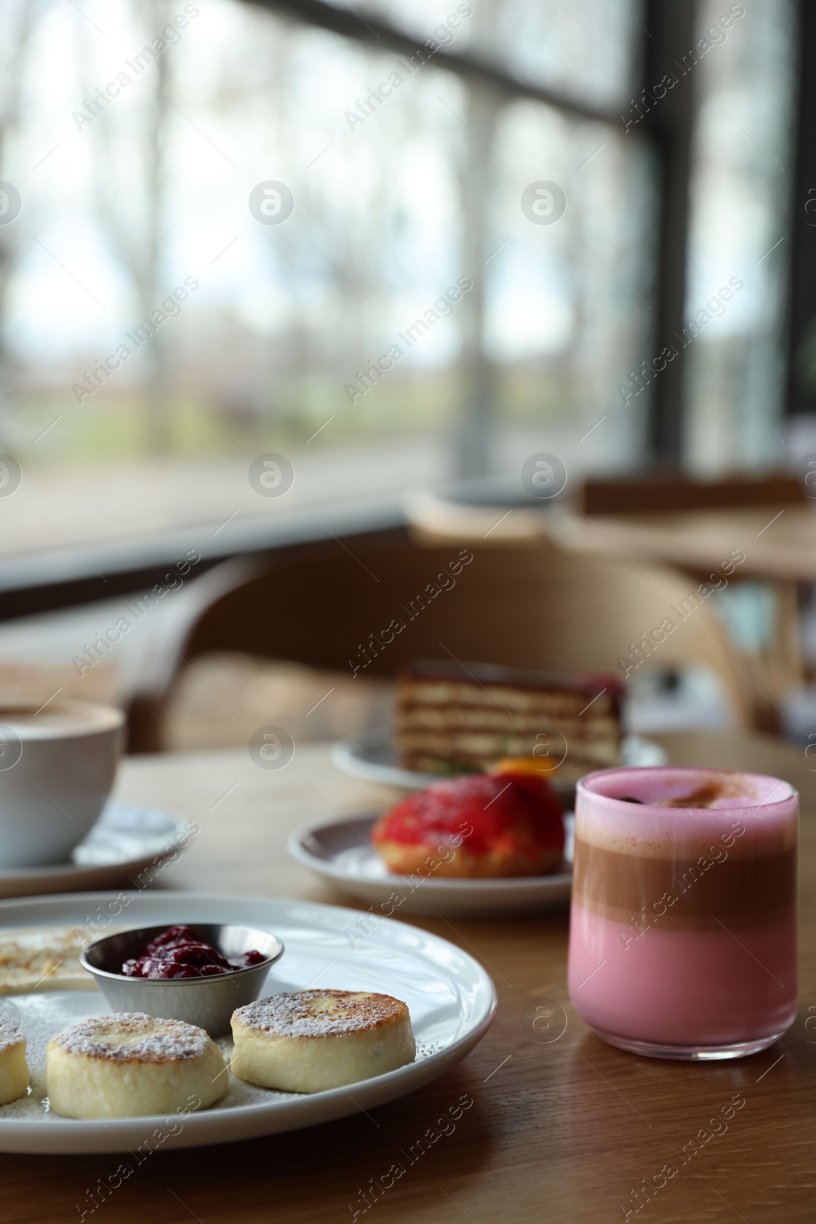 Photo of Delicious cottage cheese pancakes, desserts and aromatic coffee served on wooden table in cafe, closeup