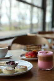 Photo of Delicious cottage cheese pancakes, desserts and aromatic coffee served on wooden table in cafe, closeup