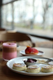 Photo of Delicious cottage cheese pancakes, desserts and aromatic coffee served on wooden table in cafe, closeup