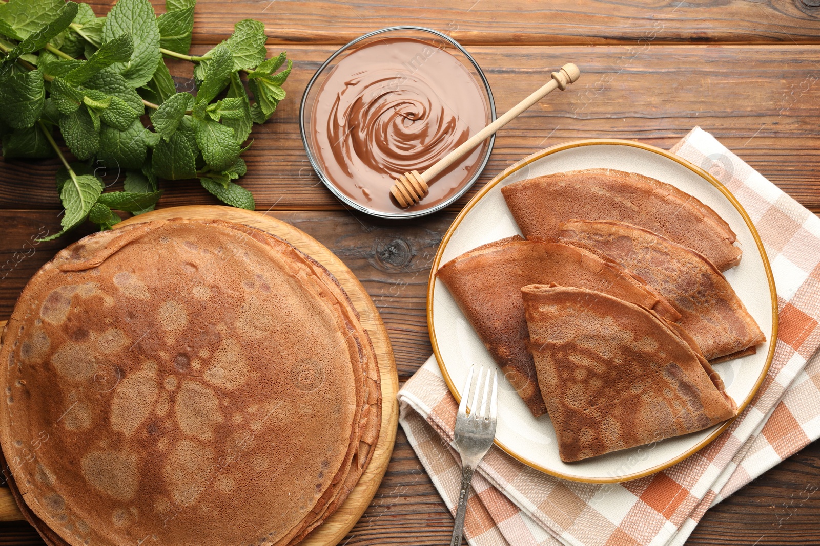 Photo of Delicious chocolate crepes, sweet sauce and mint on wooden table, flat lay