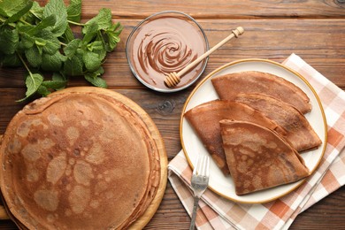 Photo of Delicious chocolate crepes, sweet sauce and mint on wooden table, flat lay