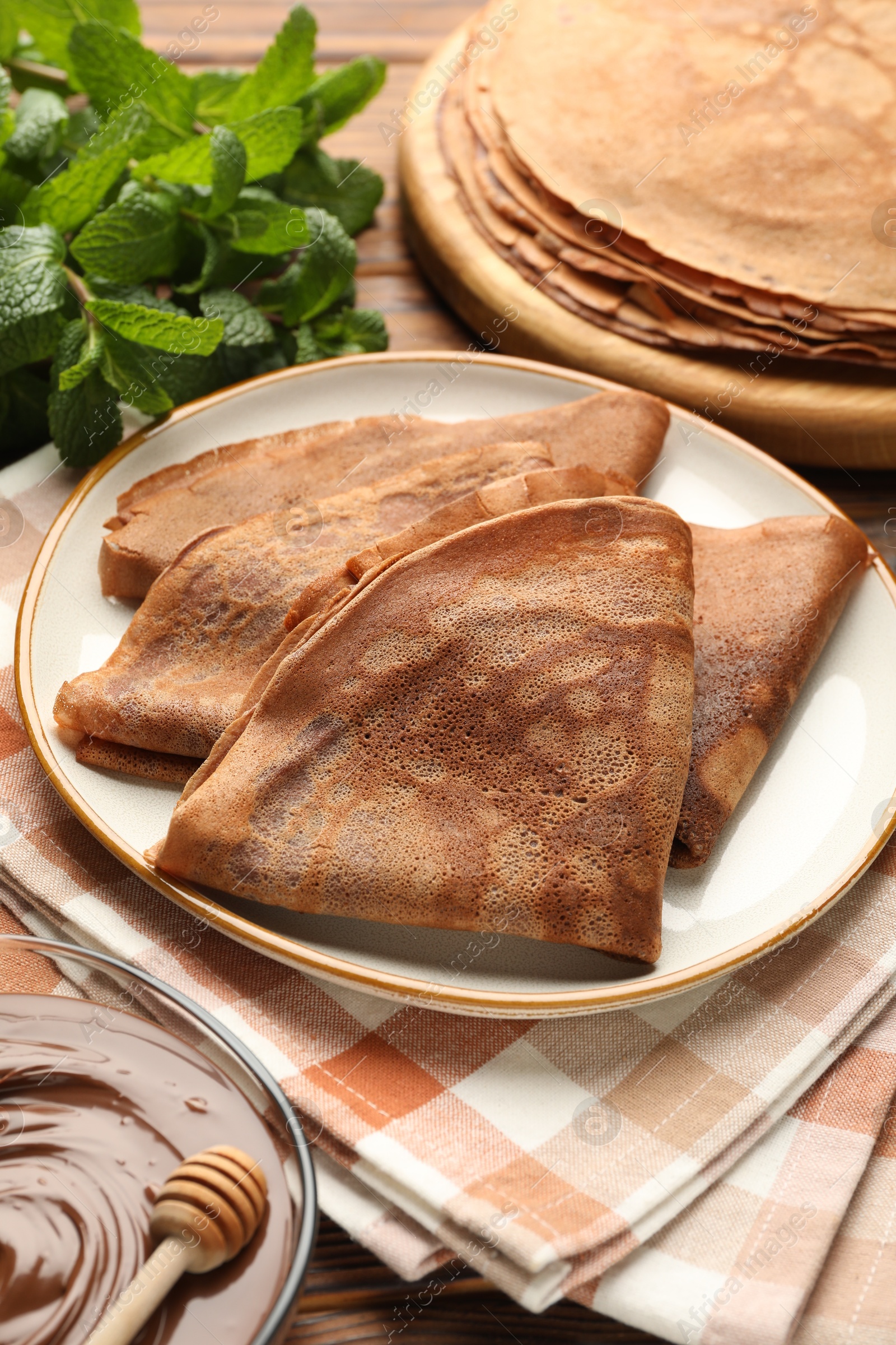 Photo of Delicious chocolate crepes, sweet sauce and mint on wooden table, closeup