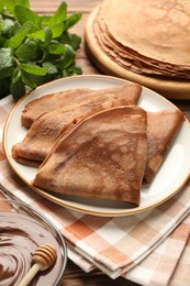 Photo of Delicious chocolate crepes, sweet sauce and mint on wooden table, closeup