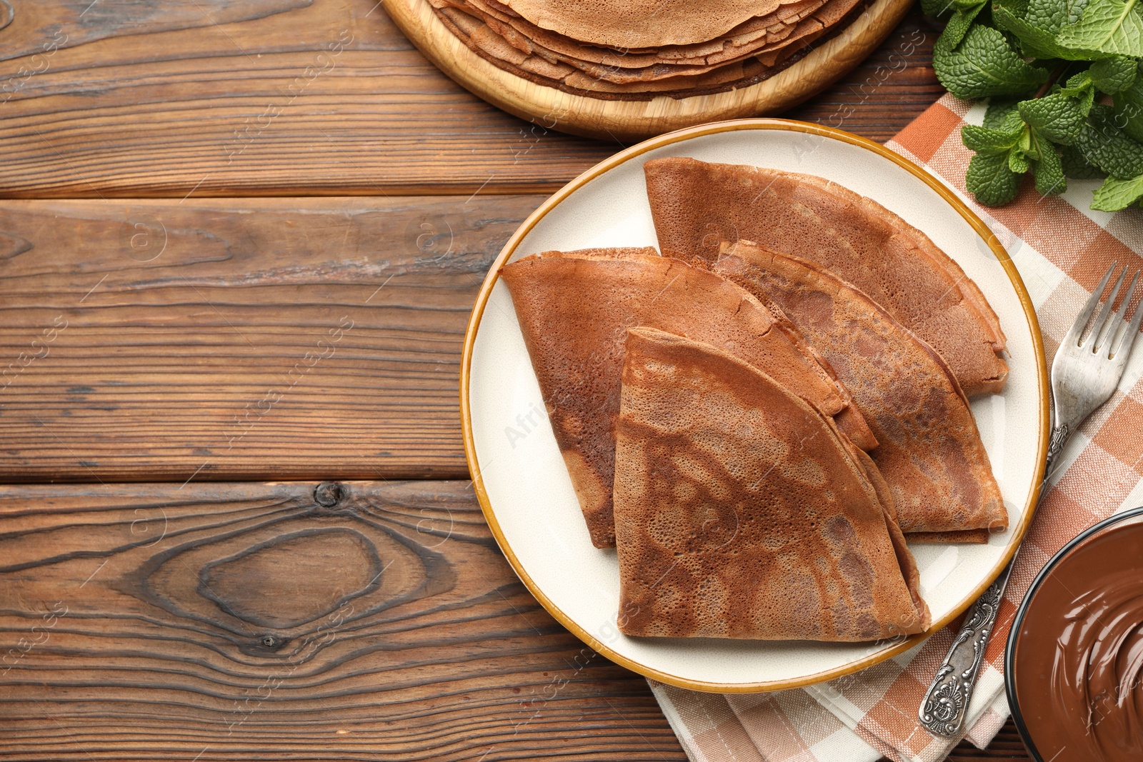 Photo of Delicious chocolate crepes, sweet sauce and mint on wooden table, flat lay. Space for text