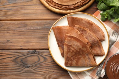 Photo of Delicious chocolate crepes, sweet sauce and mint on wooden table, flat lay. Space for text