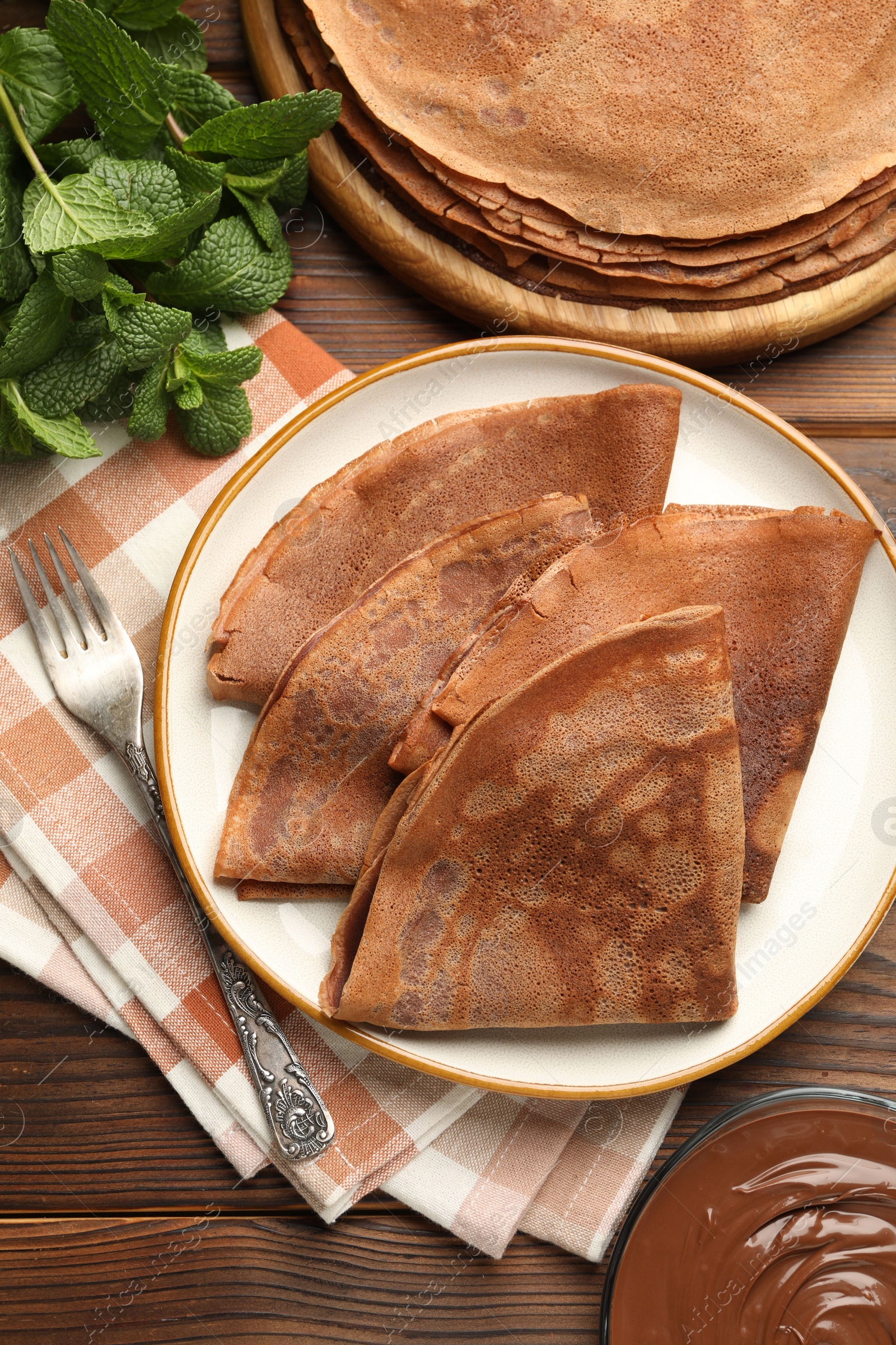 Photo of Delicious chocolate crepes, sweet sauce and mint on wooden table, flat lay