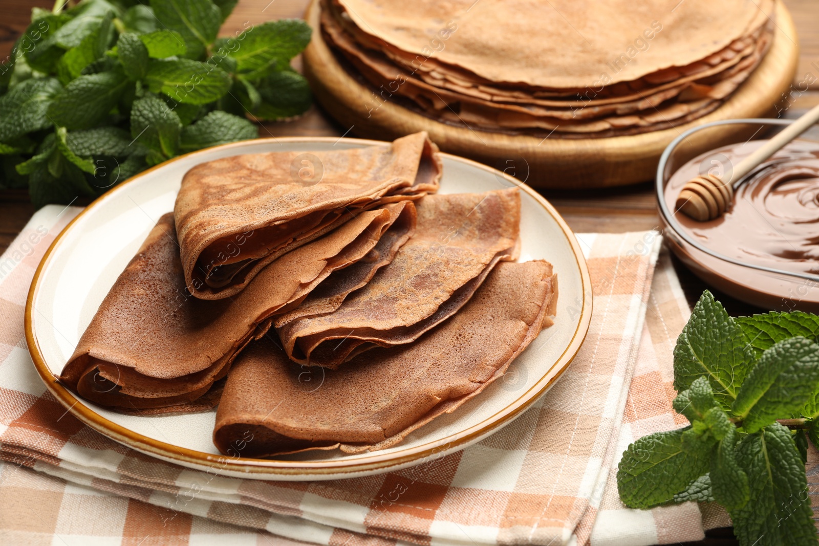 Photo of Delicious chocolate crepes, sweet sauce and mint on wooden table, closeup