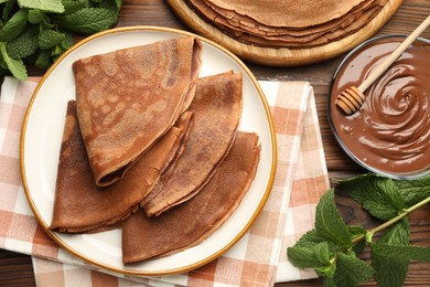 Photo of Delicious chocolate crepes, sweet sauce and mint on wooden table, flat lay