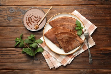 Photo of Delicious chocolate crepes, sweet sauce and mint on wooden table, flat lay