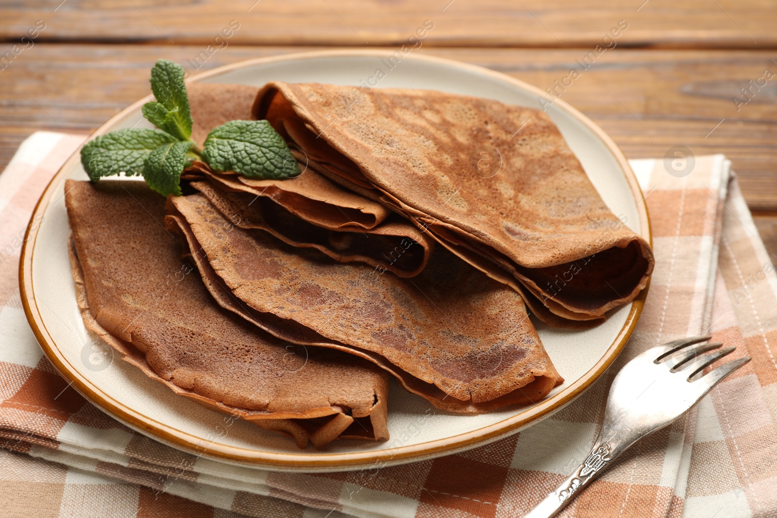 Photo of Delicious chocolate crepes and mint on wooden table, closeup