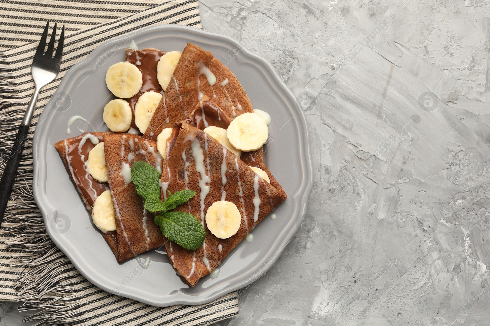 Photo of Delicious chocolate crepes with banana, condensed milk and mint served on grey table, top view. Space for text