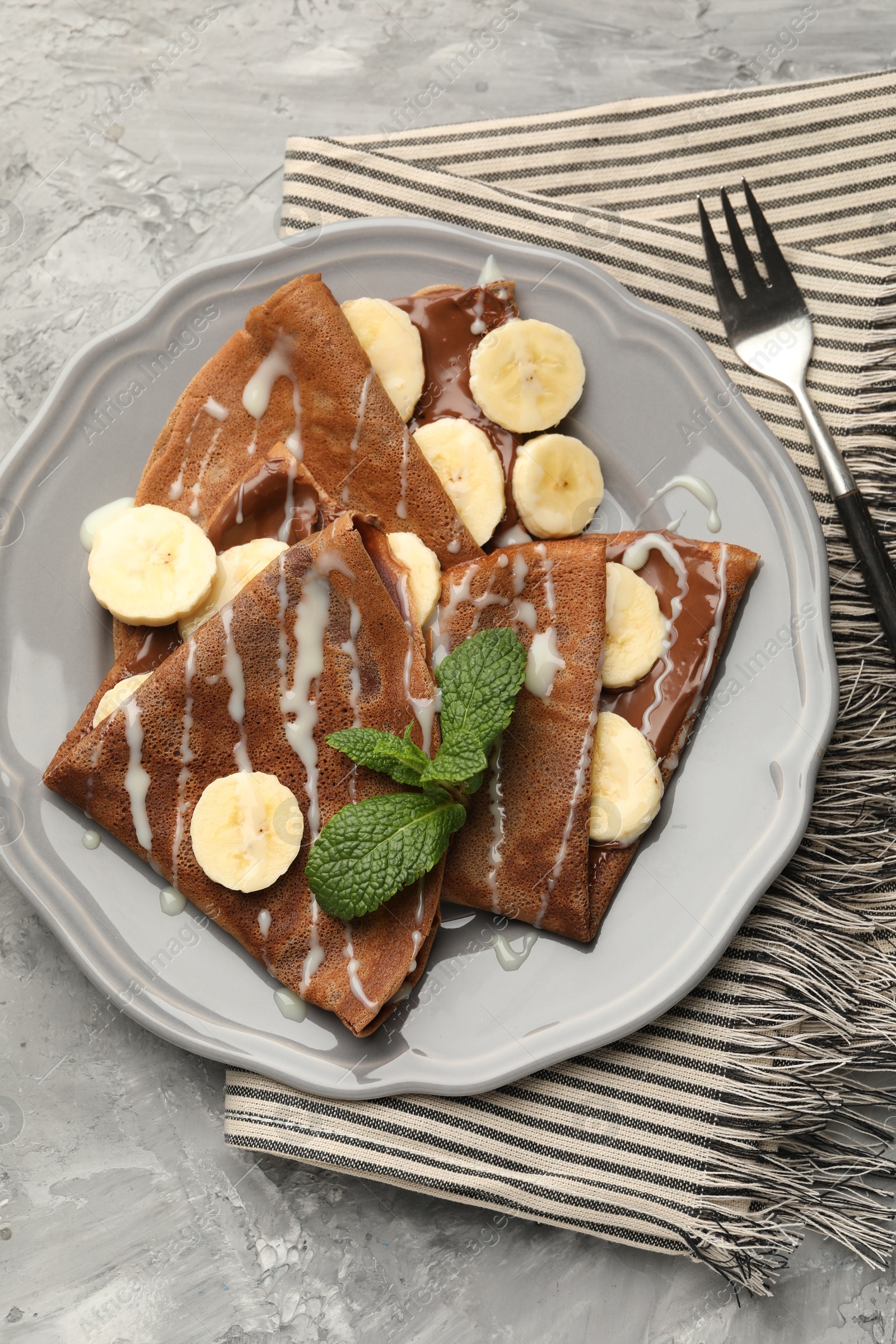 Photo of Delicious chocolate crepes with banana, condensed milk and mint served on grey table, top view