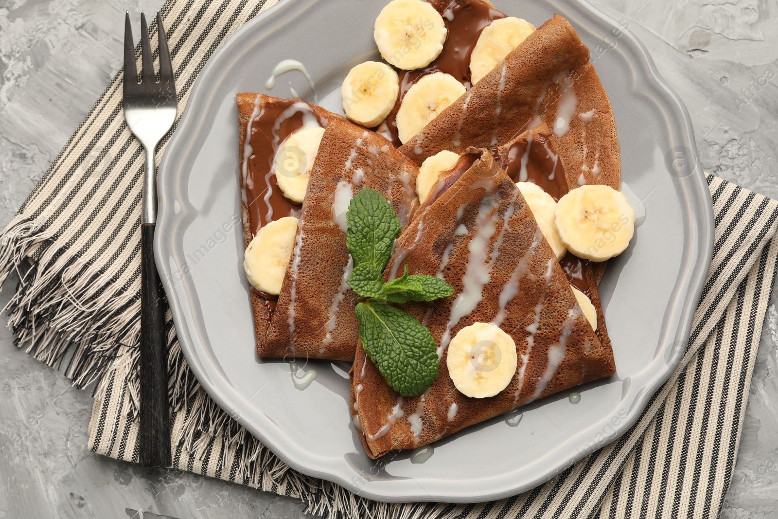 Photo of Delicious chocolate crepes with banana, condensed milk and mint served on grey table, top view